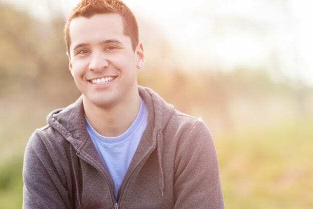 Smiling young man in a hoodie sitting outdoors in soft sunlight